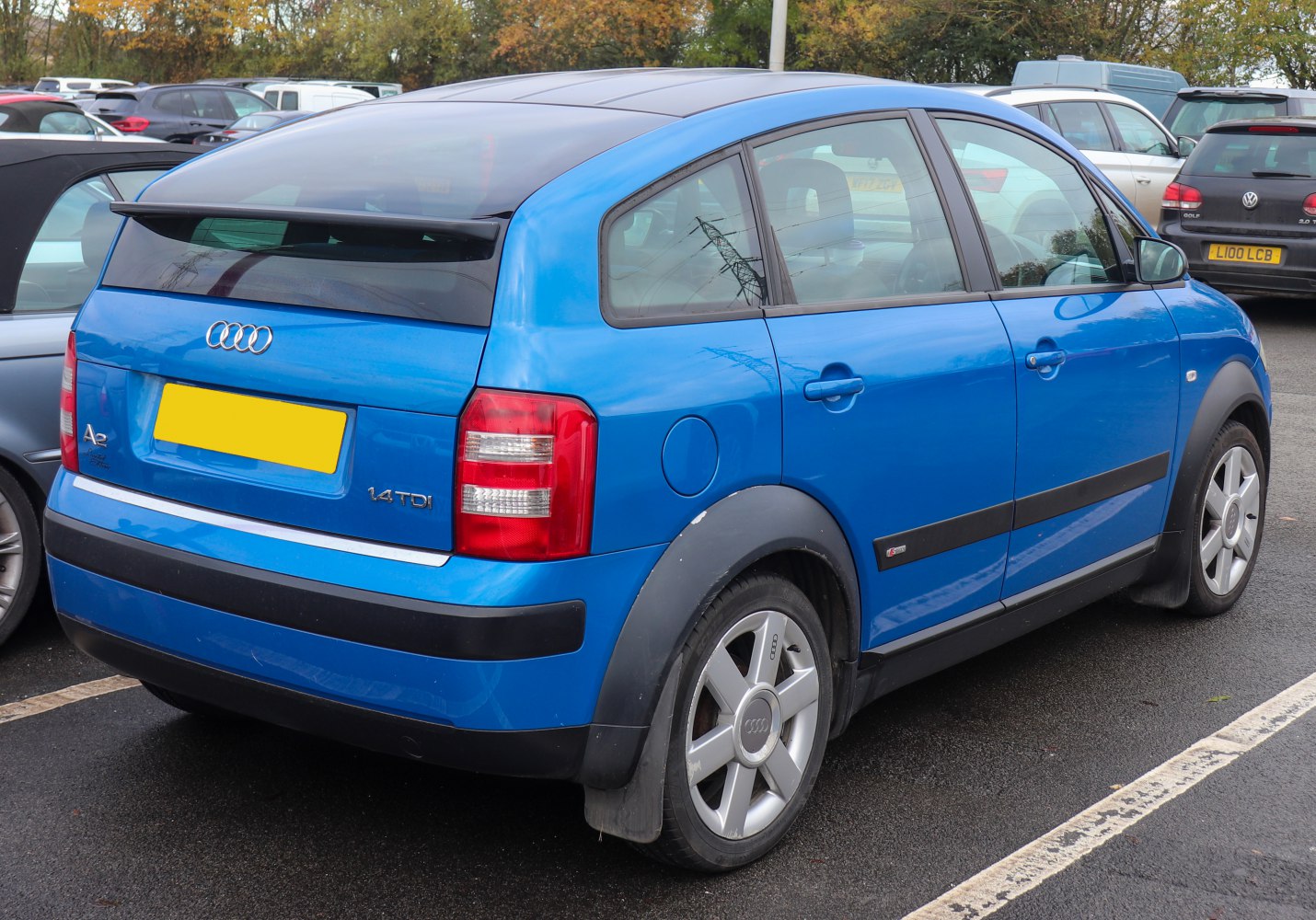 Rear-side view of blue compact hatchback with alloy wheels and rear spoiler