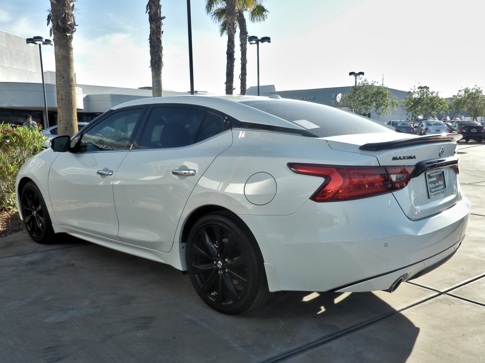 White sedan rear side view with black rims and spoiler