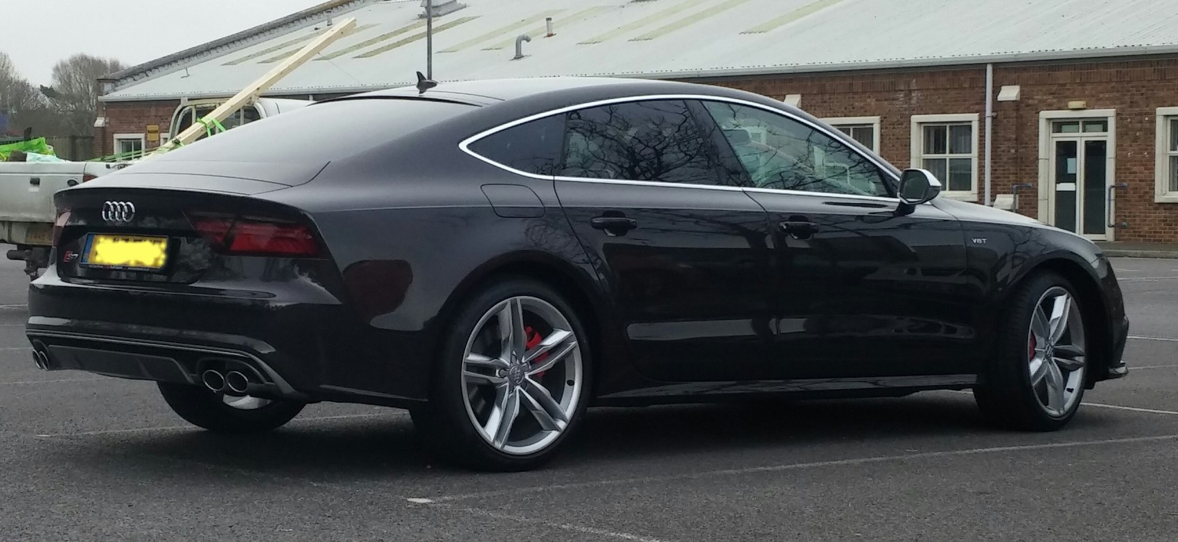 Rear-side view of a black sedan with quartz wheels and quad exhaust tips