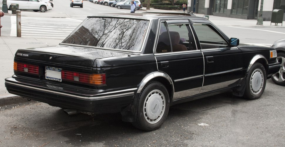 Rear side profile of a black 1980s boxy sedan with distinctive taillights and chrome trim.