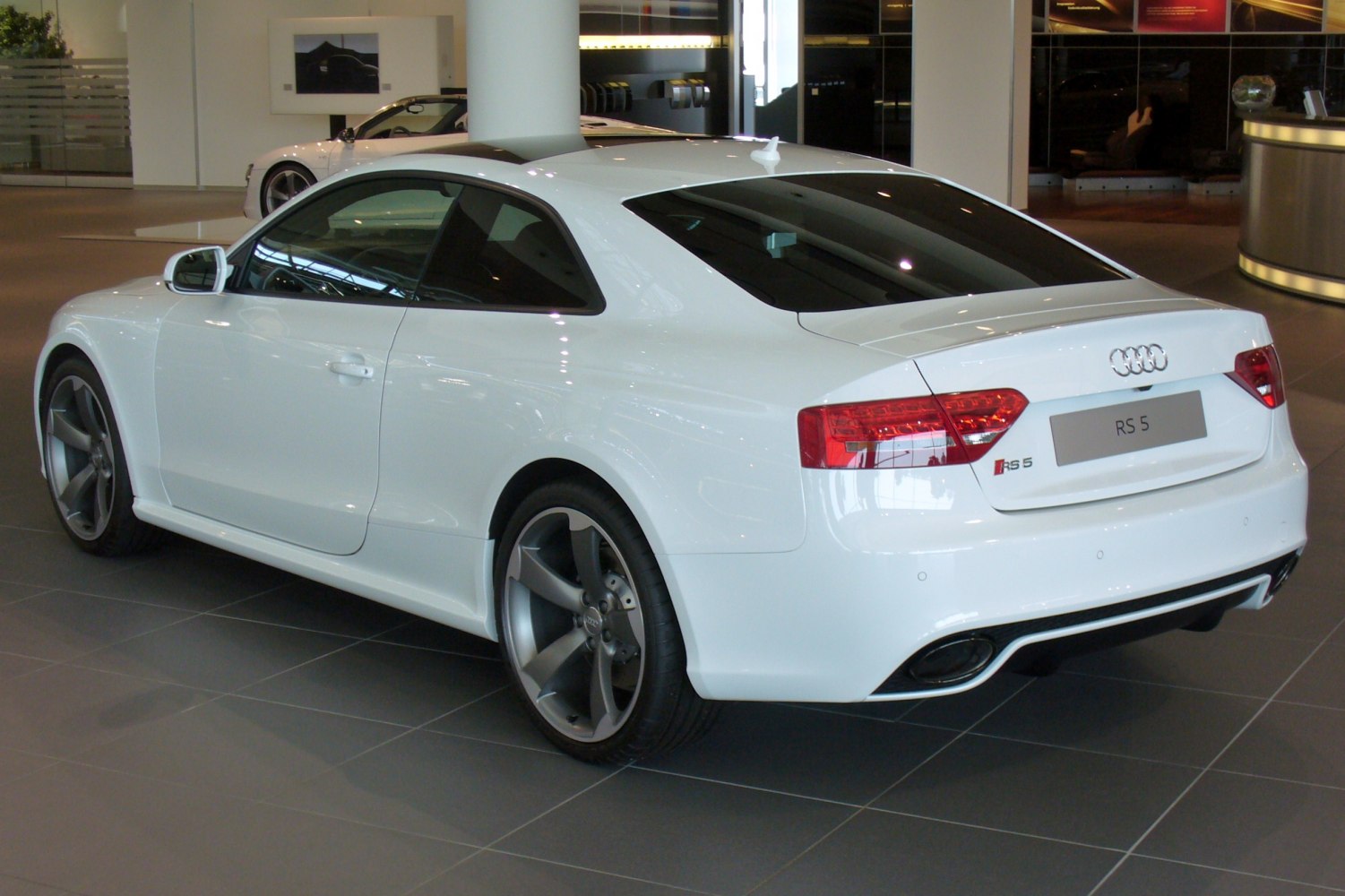 Rear and side view of a white coupe with tinted windows and 5-spoke alloy wheels.