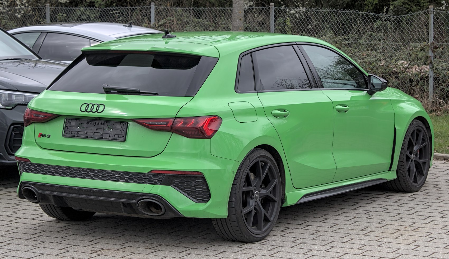 Rear and side view of green sporty hatchback with black wheels and dual exhaust