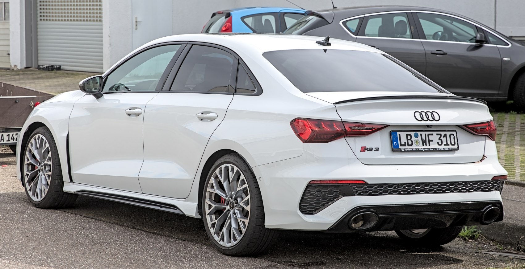 Rear-side view of a white sedan with dual exhaust and alloy wheels