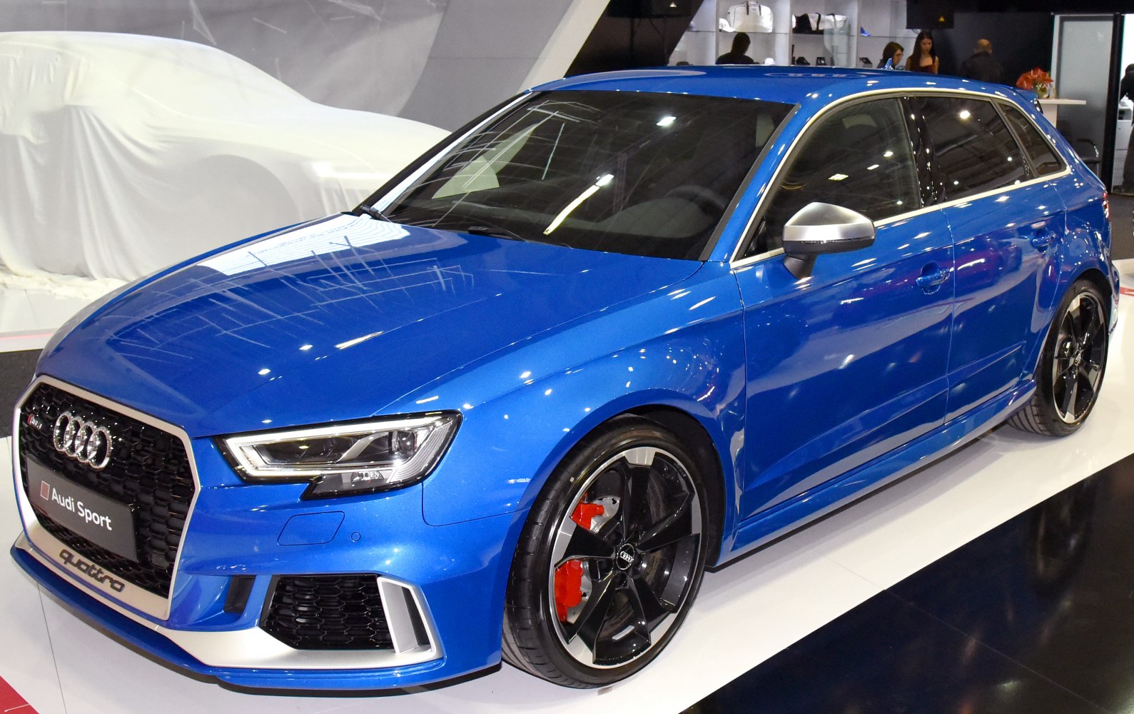 Black alloy wheels with red brake calipers on a blue sporty hatchback.