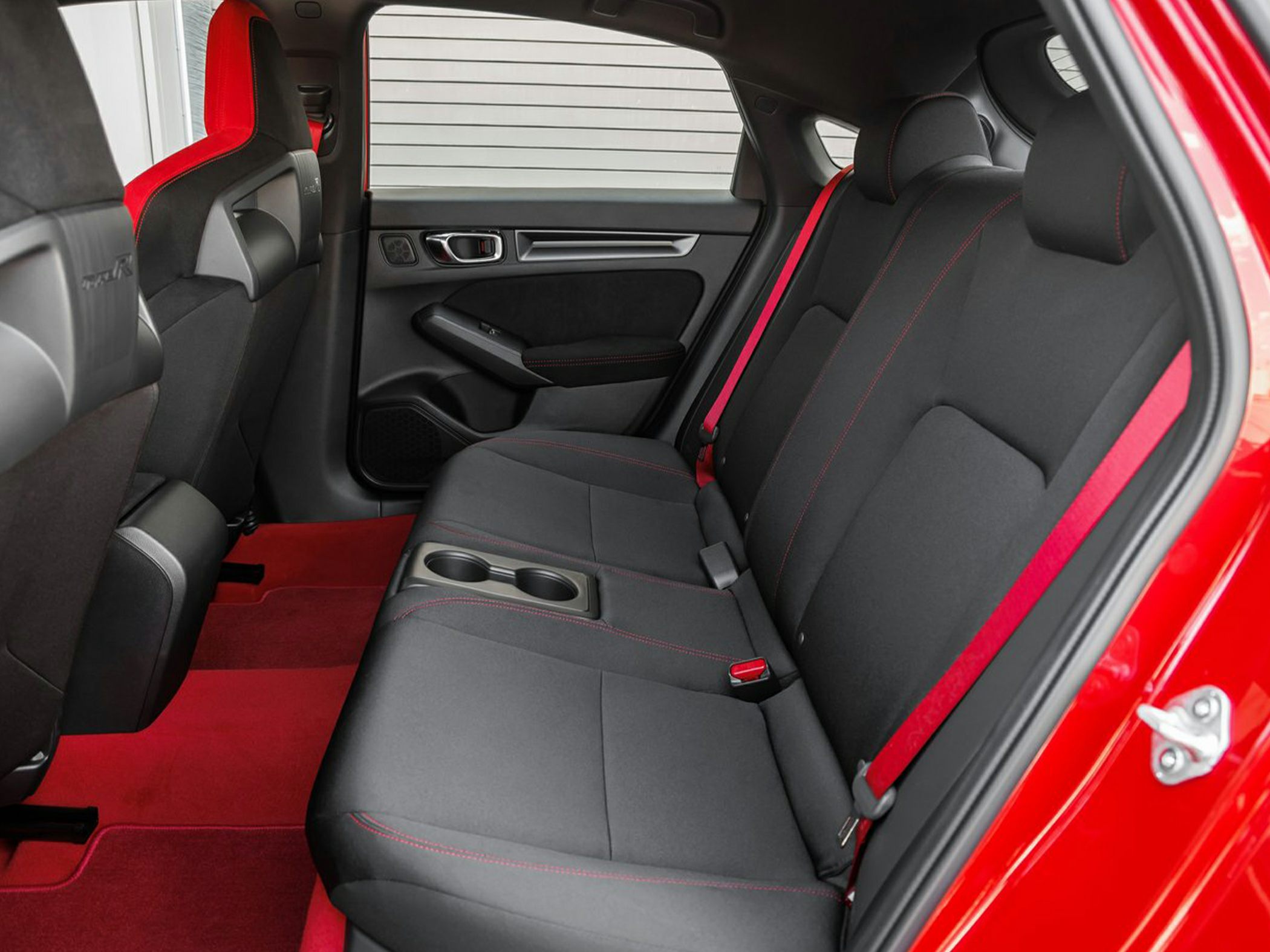 Rear seat interior with sporty black upholstery and red accents including seat belts and floor mats.