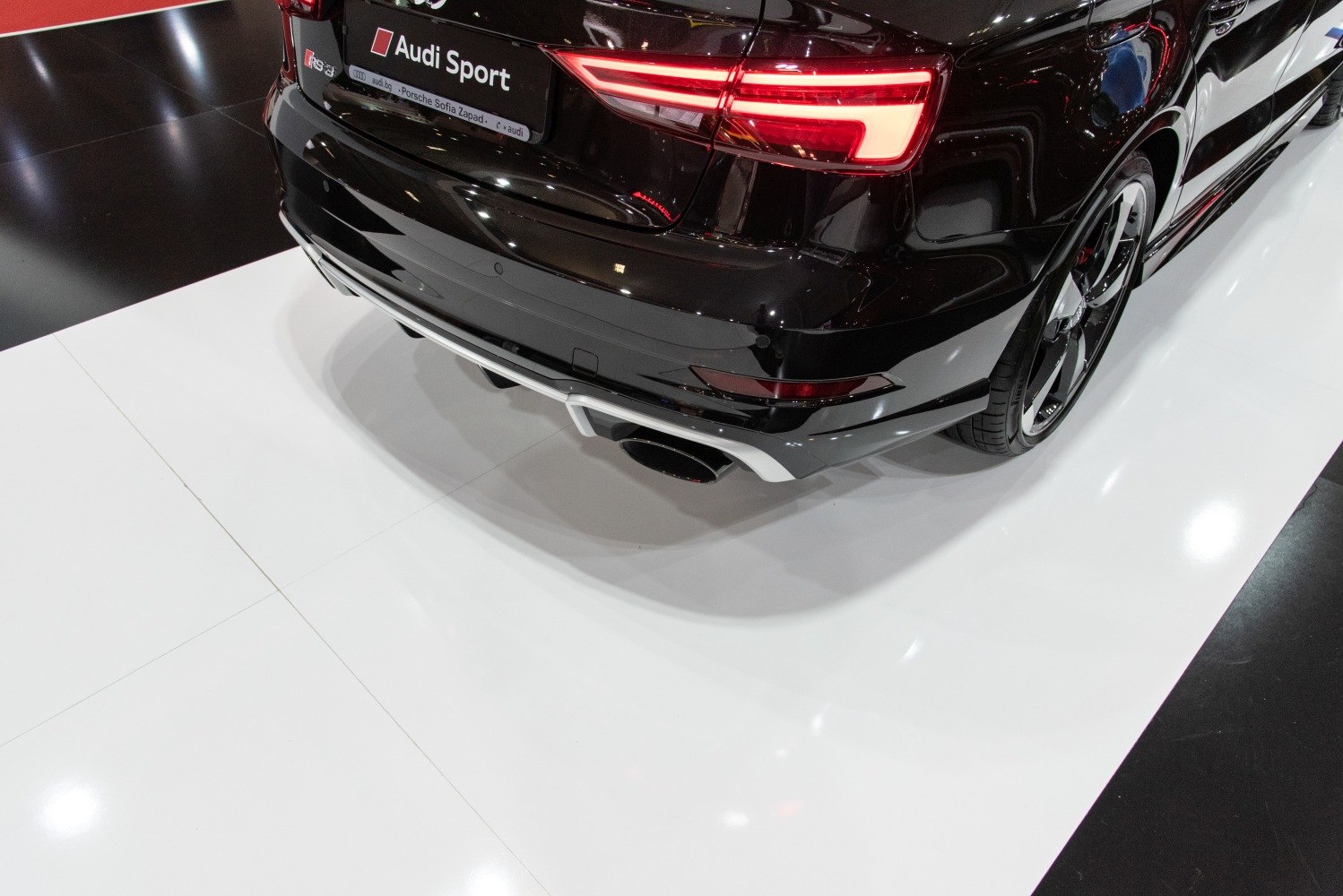 Rear end with LED tail light and sporty exhaust of a black sedan.