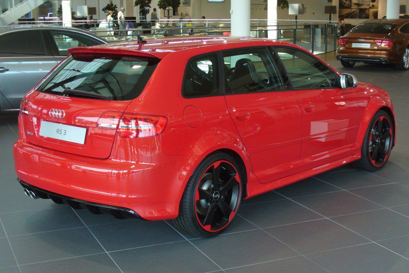 Red sporty hatchback with black alloy wheels and dual exhaust pipes