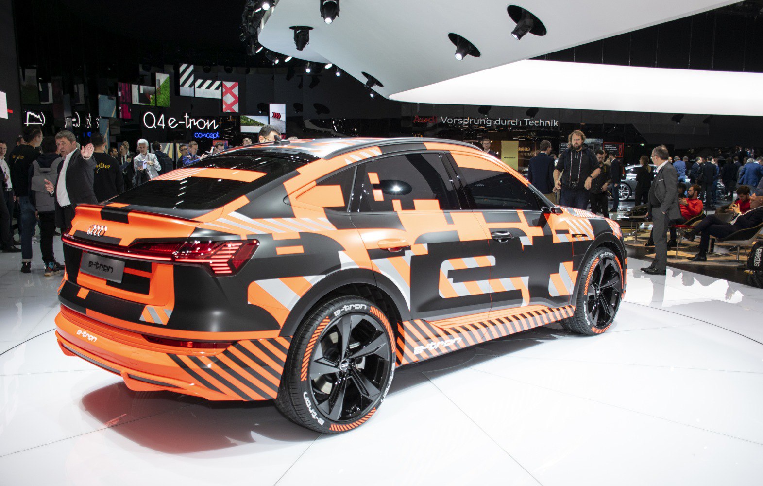 Rear design of an electric SUV with black and orange camouflage wrap and distinctive black alloy wheels.