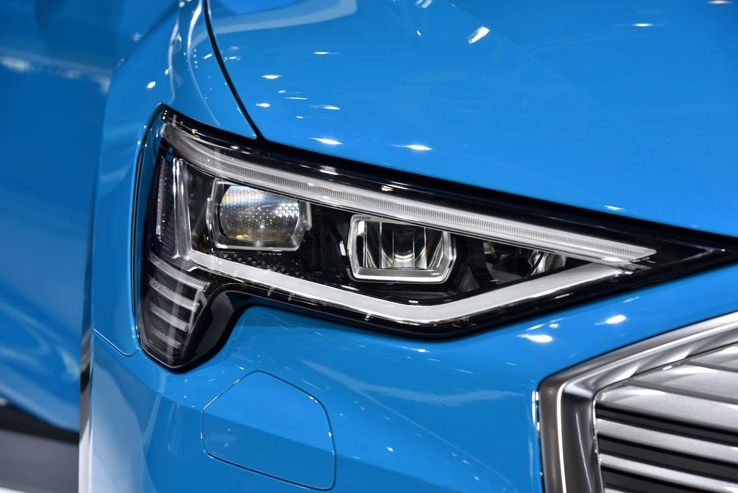 Close-up of Audi e-tron 2019 LED headlight and grille corner in blue.