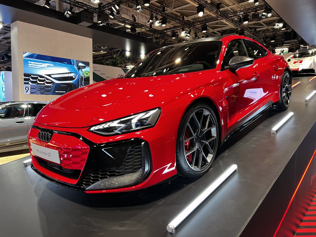 Red electric sports sedan with sharp LED headlights and sporty alloy wheels.