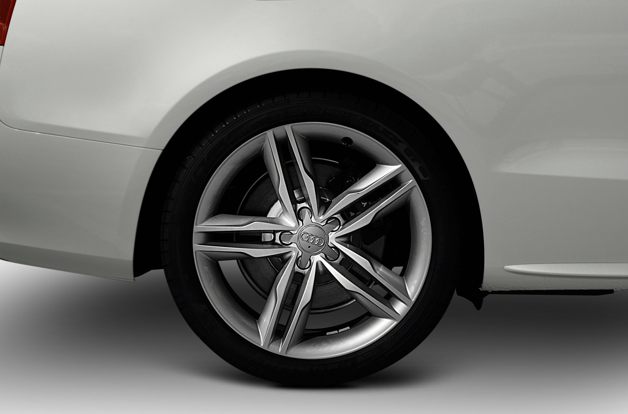 Close-up of a 5 twin-spoke alloy wheel rim and brake disc on a white car.