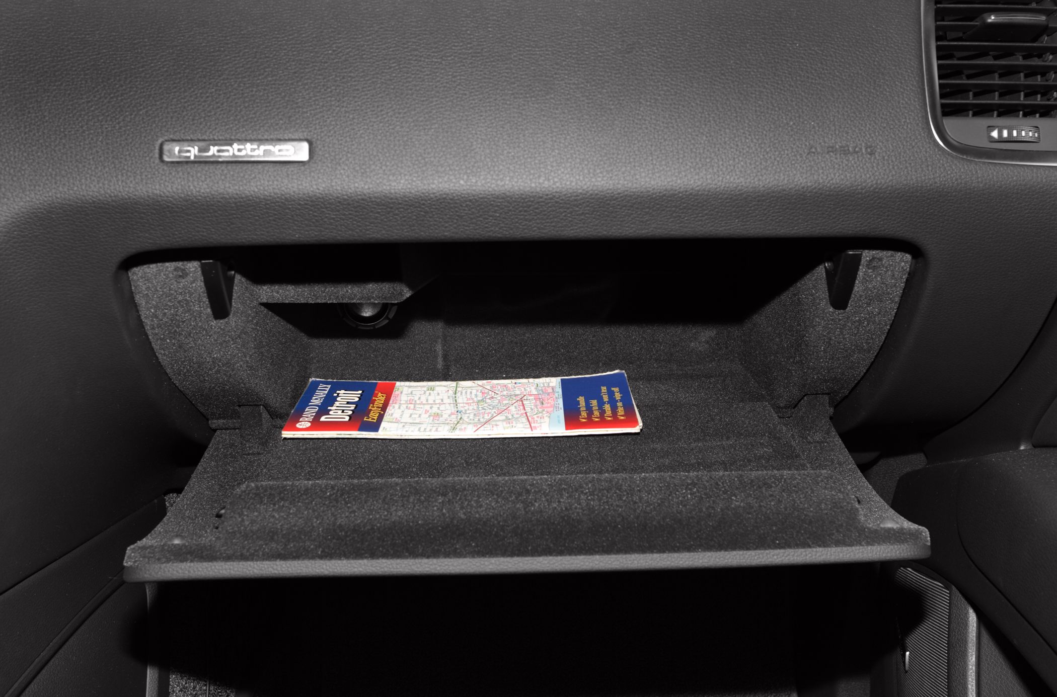 Open glovebox with a road map inside and quattro badge on dashboard