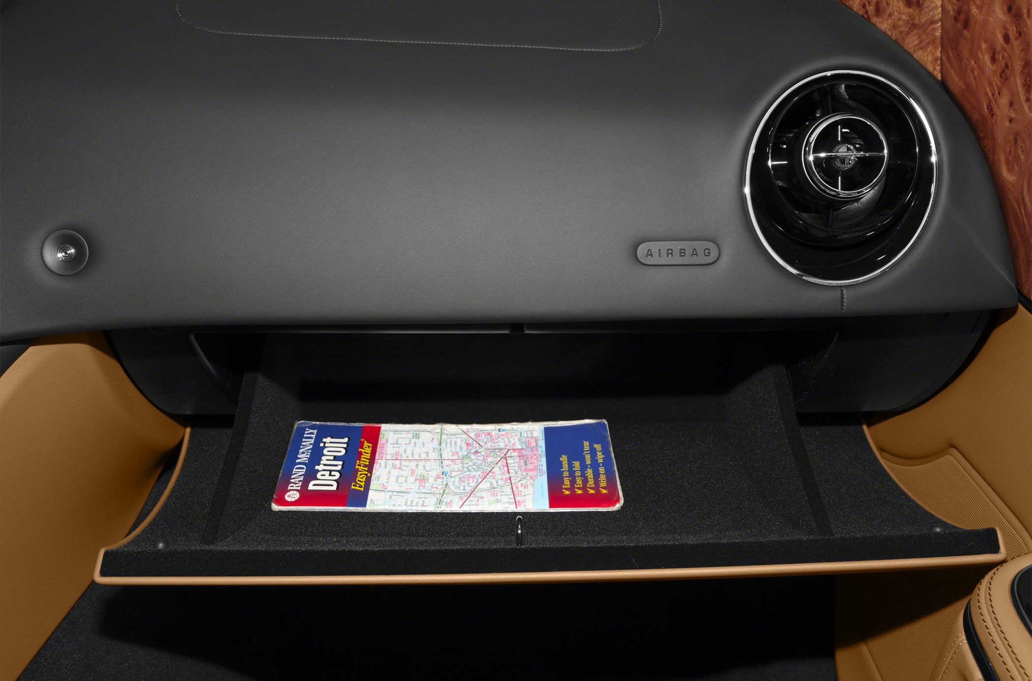Dashboard glove box with ventilation and airbag on tan and black interior.