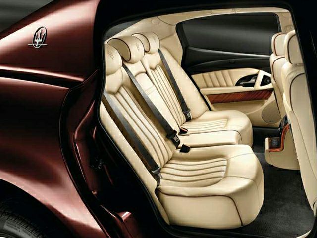 Beige leather rear seats with wood trim and seat belts in a luxury sedan