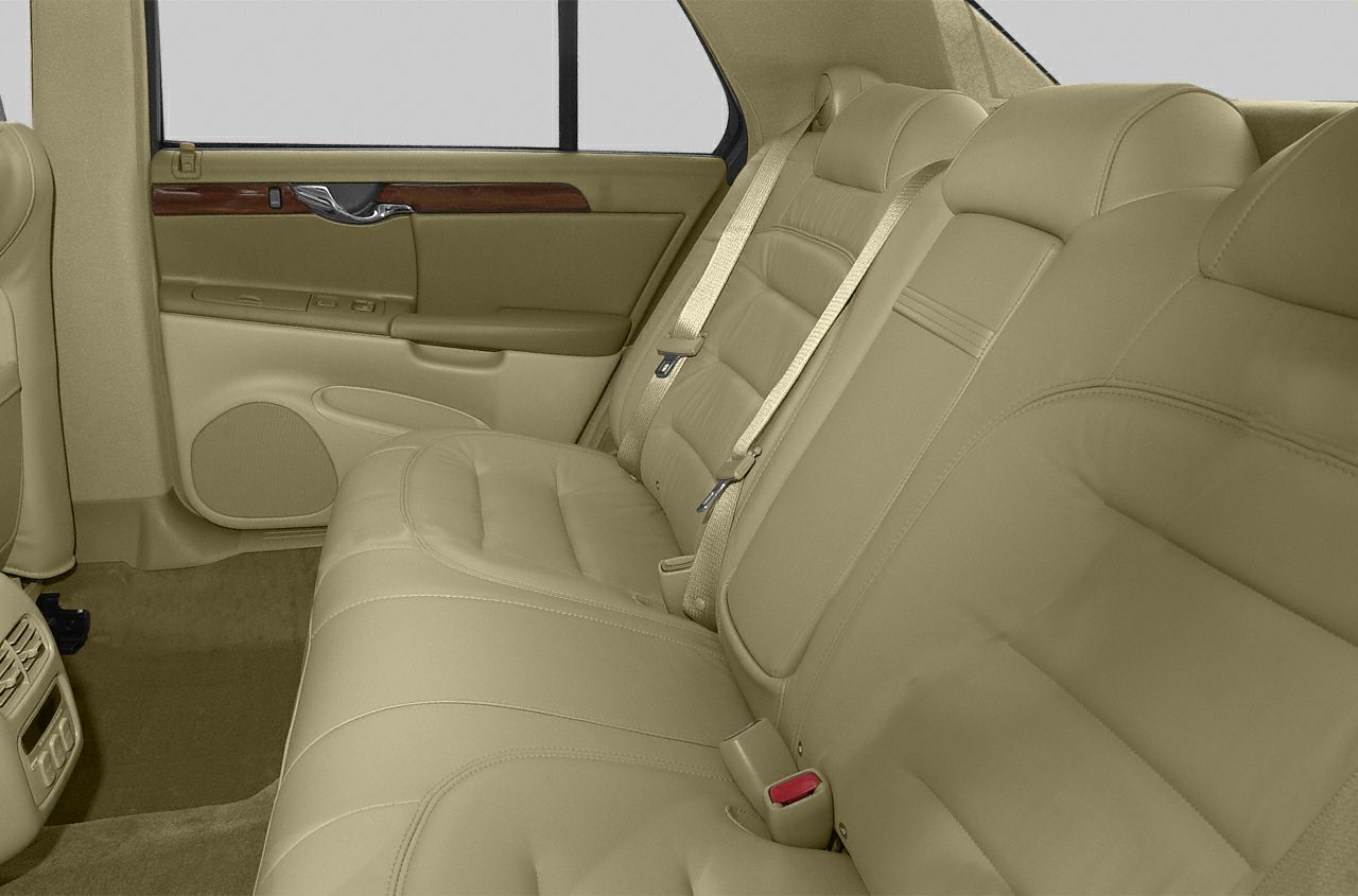 Beige leather rear seat with wood trim and seat belts.