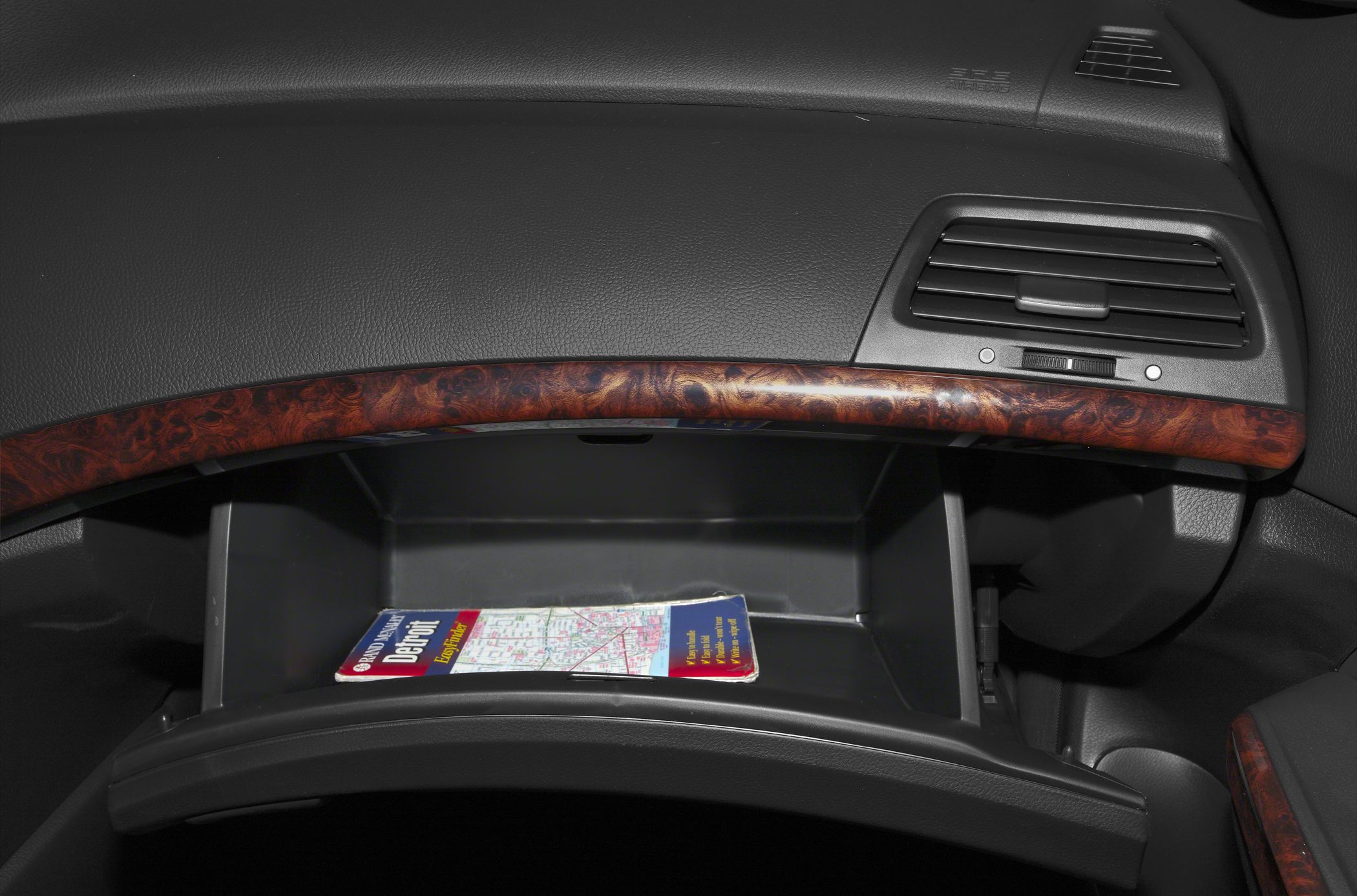 Open glove compartment with wood grain dashboard trim and air vent.