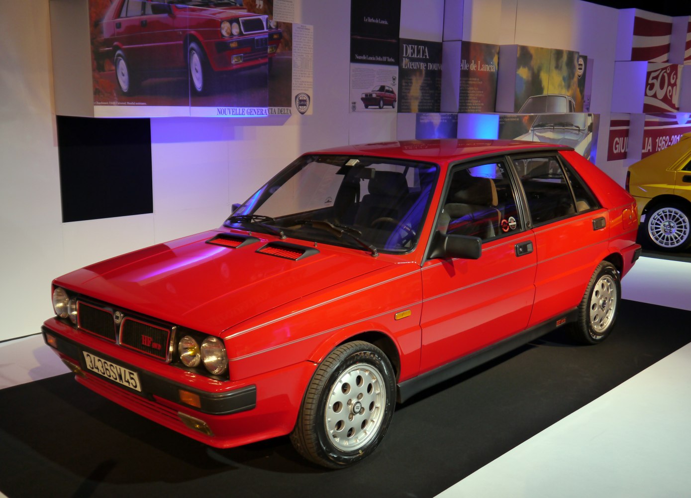 Red hatchback with dual round headlights and sporty hood vents