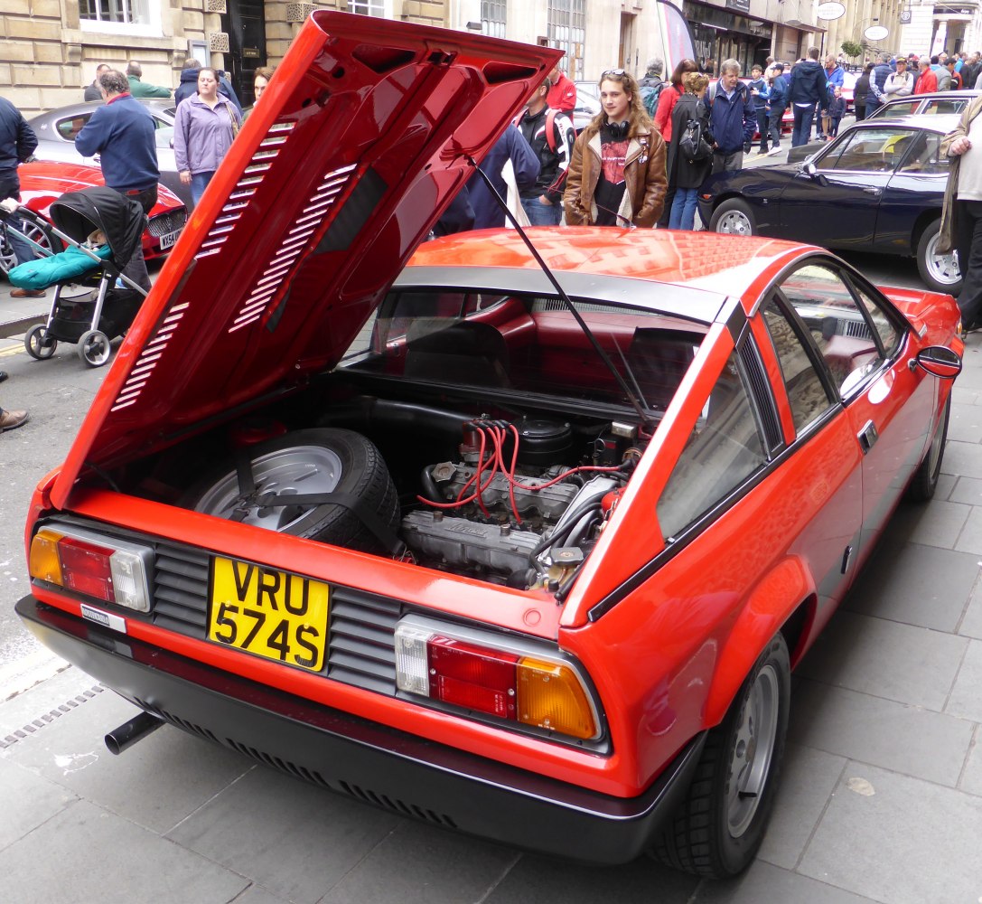Rear hatch open showing rear engine and spare tire in a vintage sports coupe