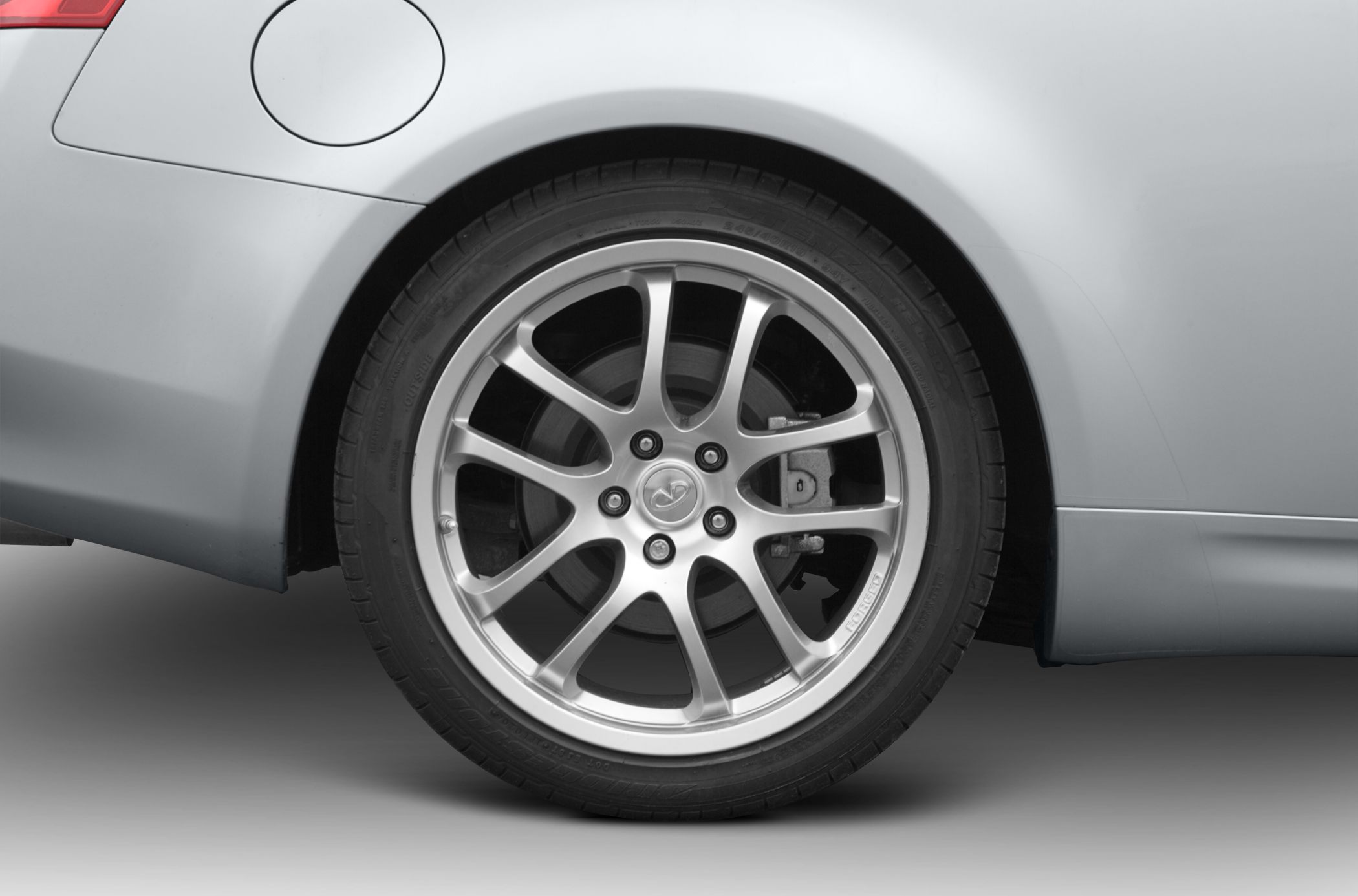 Alloy rear wheel with brake caliper and nearby fuel door on silver car panel