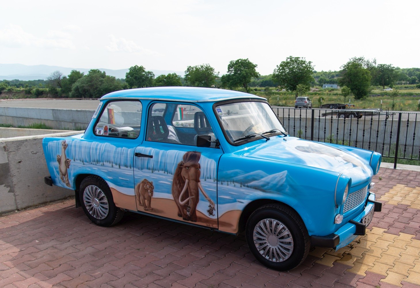 Vintage small car with detailed Ice Age animal murals and icy landscape painting.