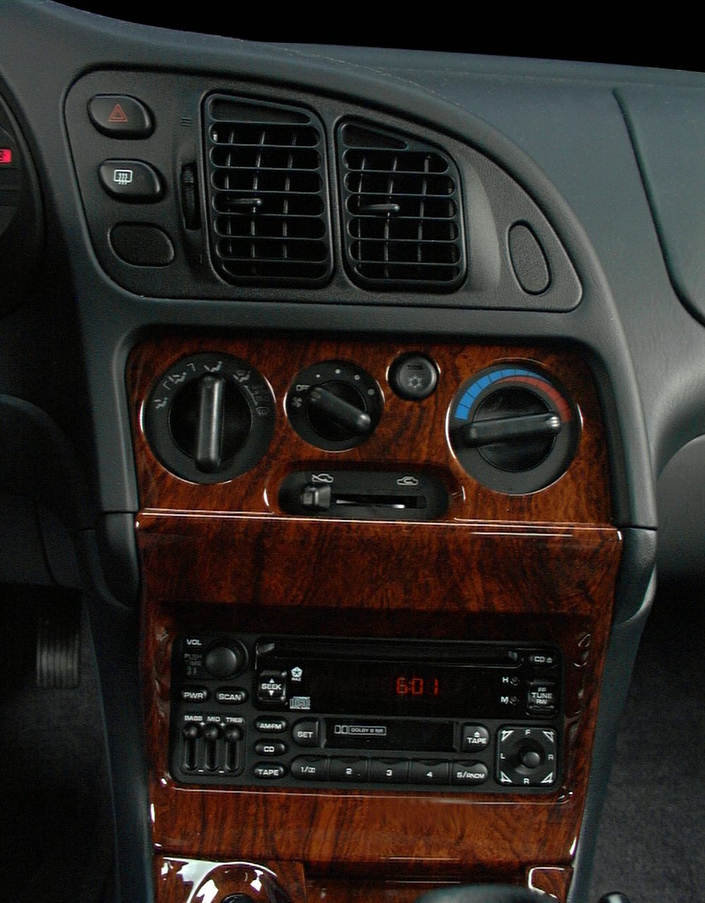 Car dashboard with air vents, climate control knobs, and vintage audio system with wood trim