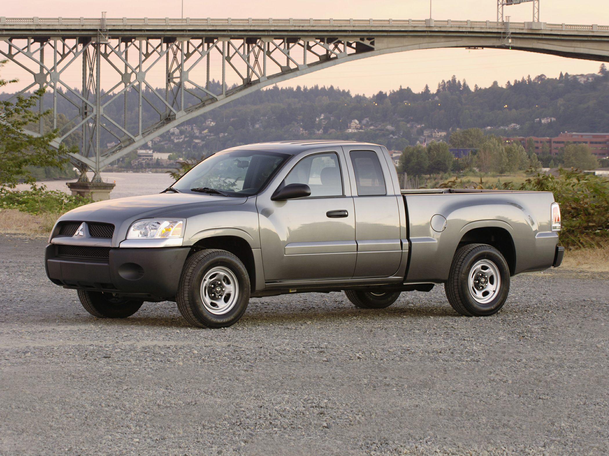 Silver extended cab pickup truck parked on gravel near a bridge