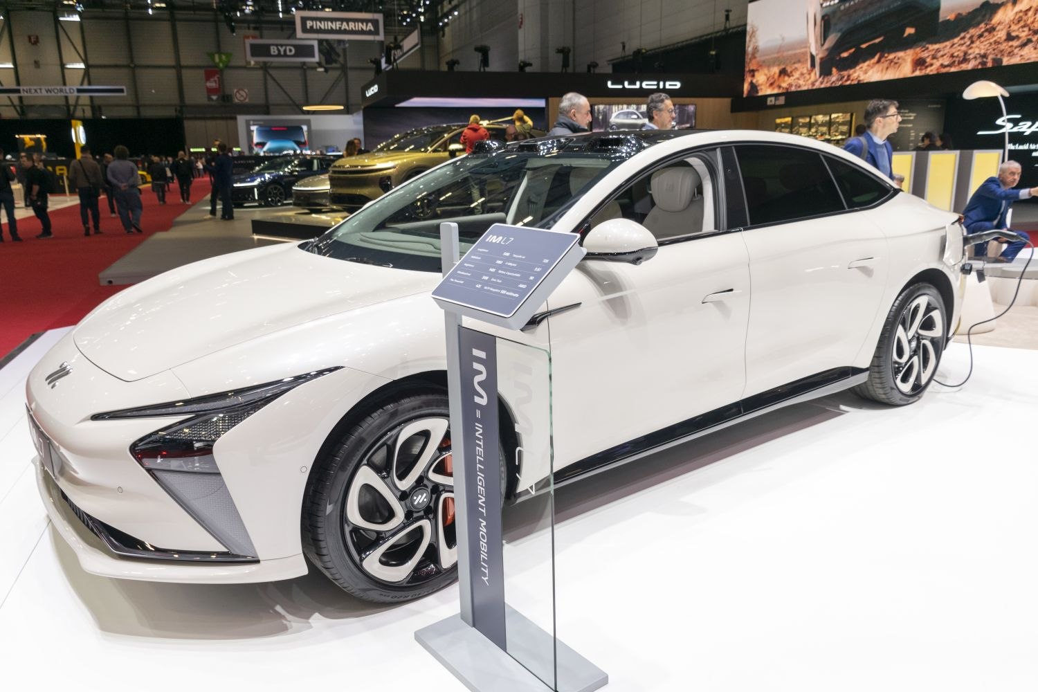 White electric sedan with aerodynamic design and LED headlights charging at exhibit