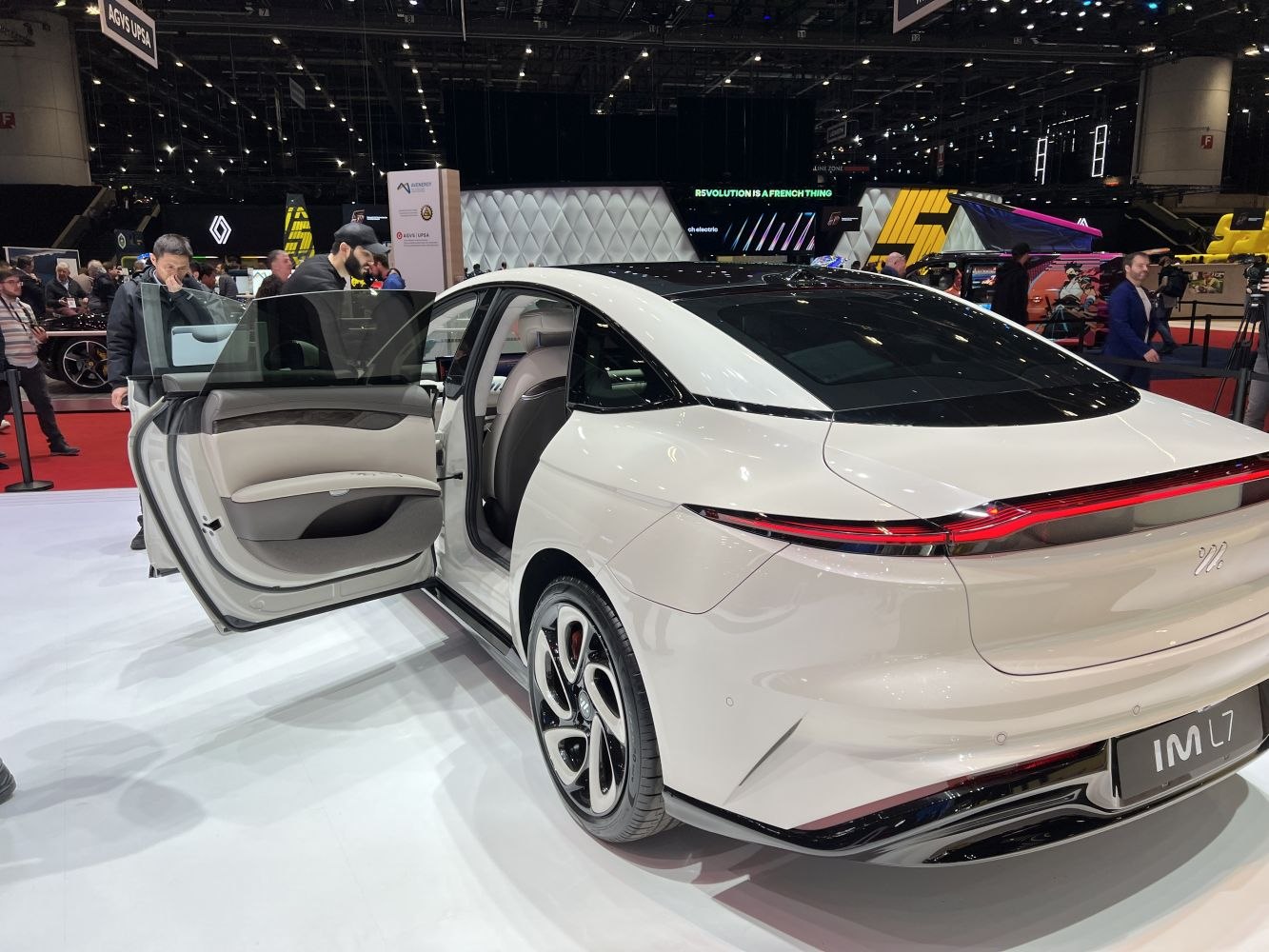 Rear view of white electric sedan with open rear door and continuous LED taillight.