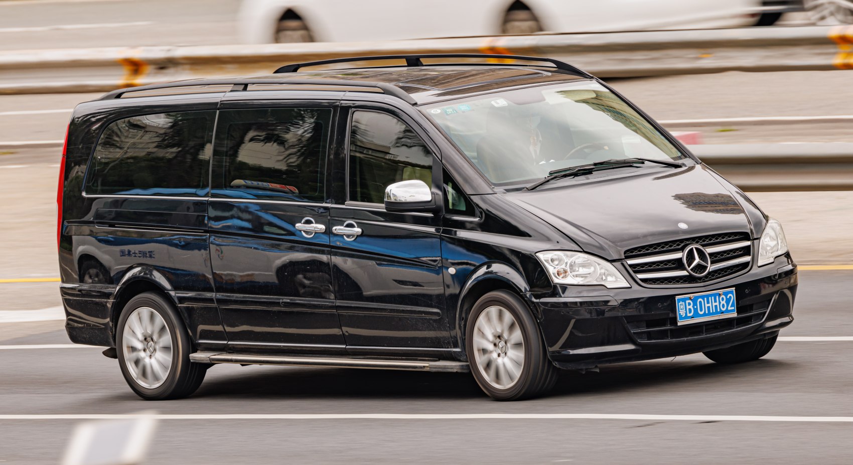 Black minivan with sliding side doors and roof rails driving on road