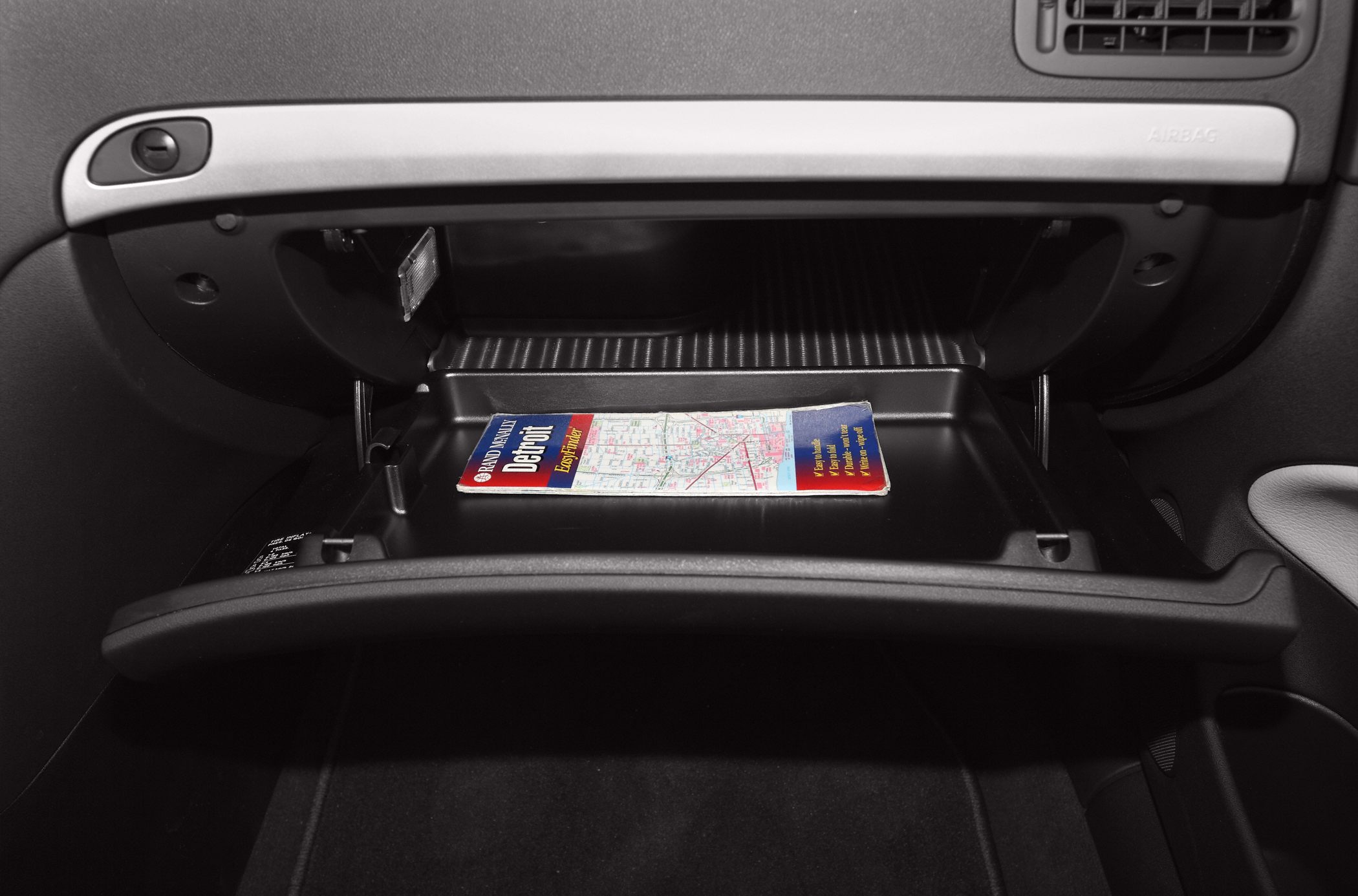 Open glove compartment with a map inside in a car interior.