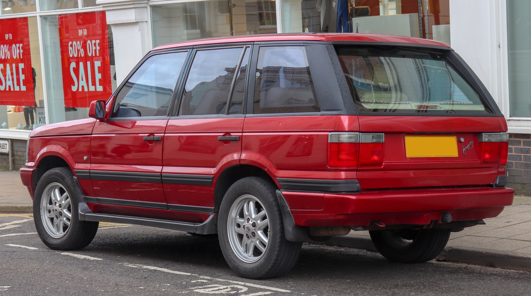Rear-side view of a red mid-90s luxury four-door SUV with alloy wheels.
