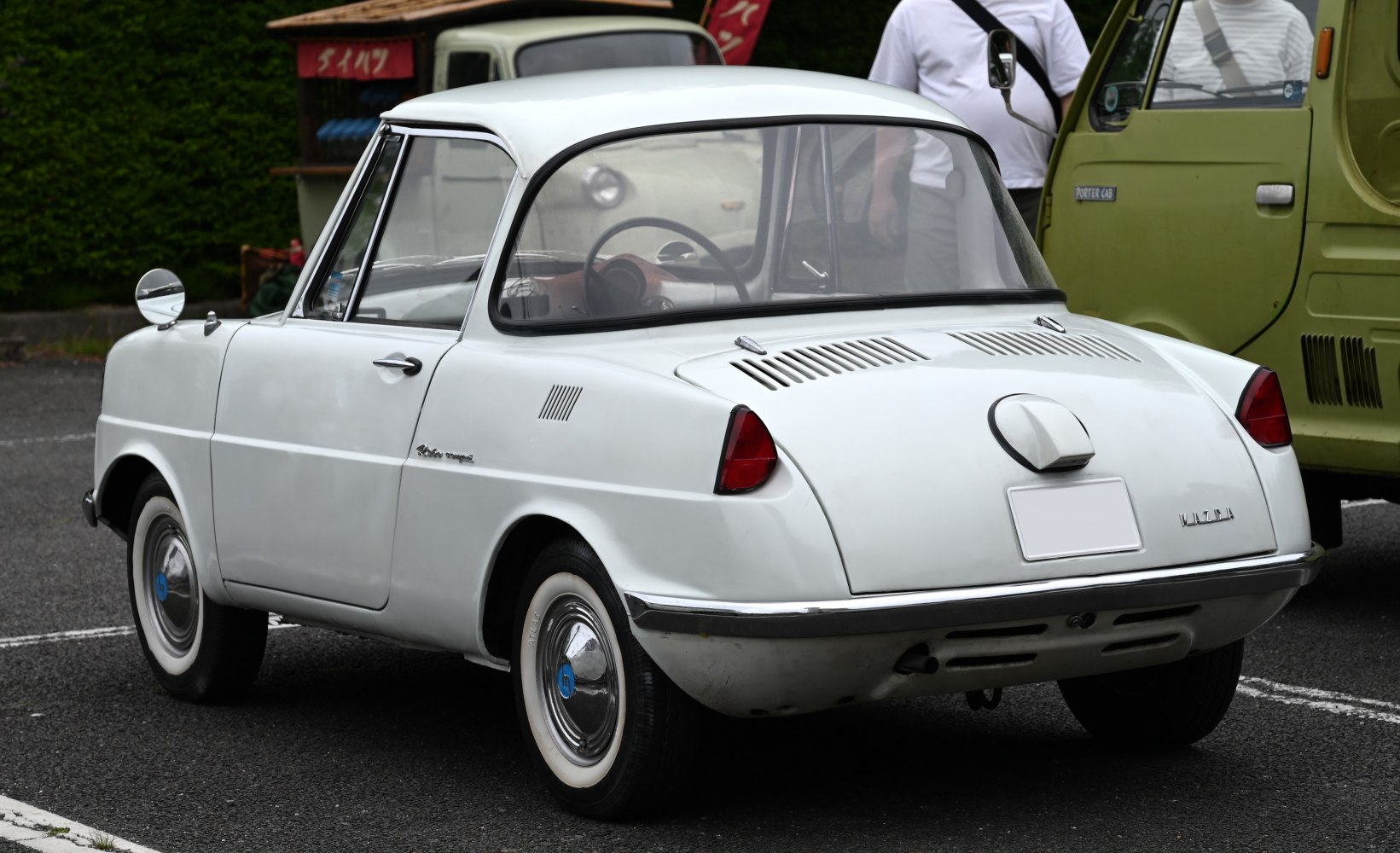 Rear view of vintage compact coupe with vented engine cover and round side mirror.
