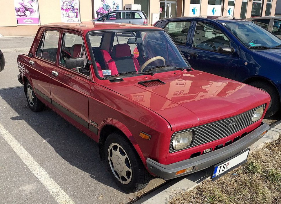 Red boxy sedan front and side view with rectangular headlights and steel wheels