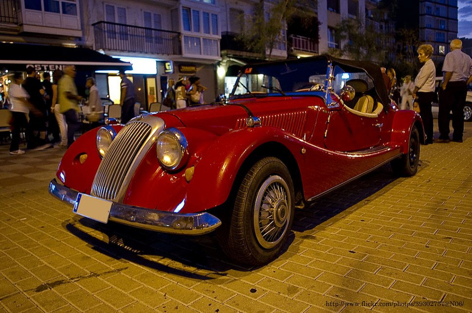Red vintage convertible with chrome grille and round headlights at night