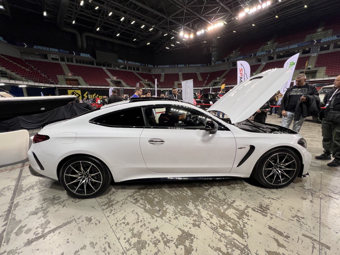 White two-door coupe with open hood and sporty alloy wheels