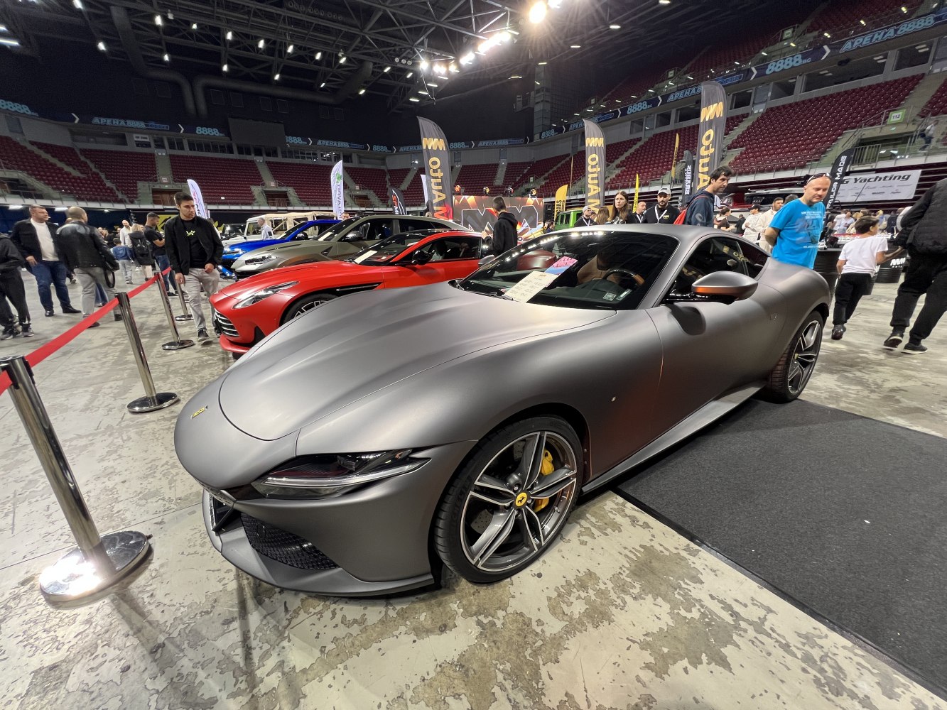 Matte gray sports coupe with aerodynamic hood and alloy wheels at indoor show