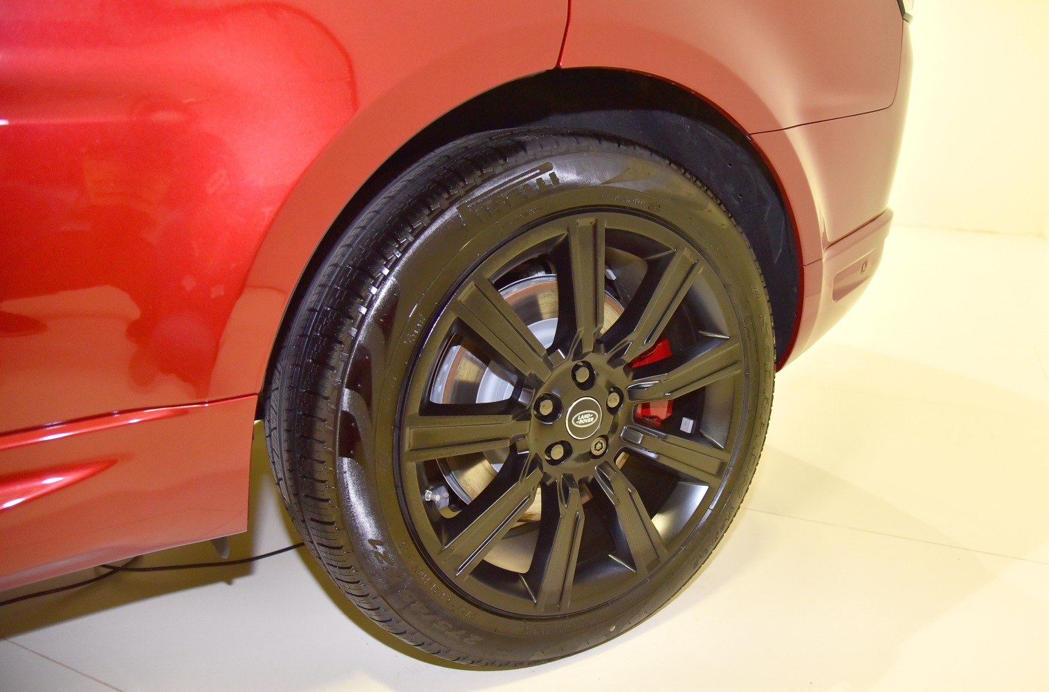 Black alloy wheel with red brake caliper on red vehicle body