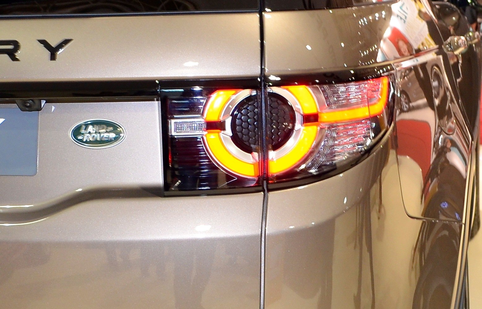 Rear circular illuminated tail light and Land Rover badge on a metallic body