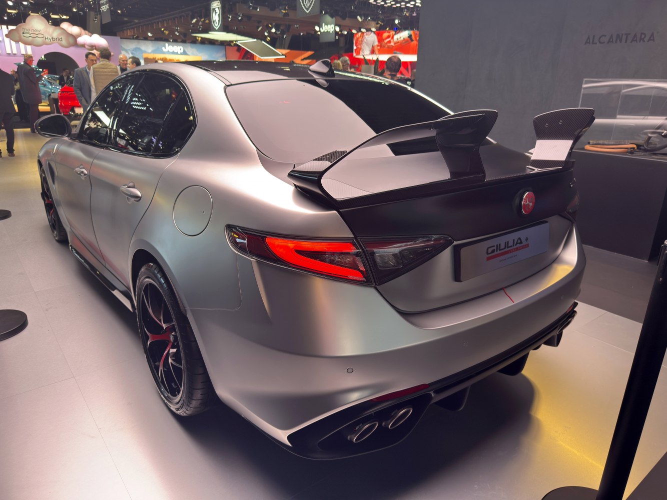 Rear view of a matte finished sedan with carbon fiber wing and quad exhaust