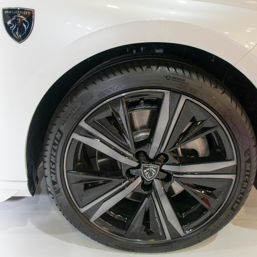 Black multi-spoke alloy wheel with Peugeot badge and white car body