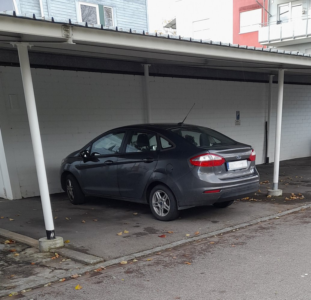 Compact sedan rear side with distinctive taillights under carport