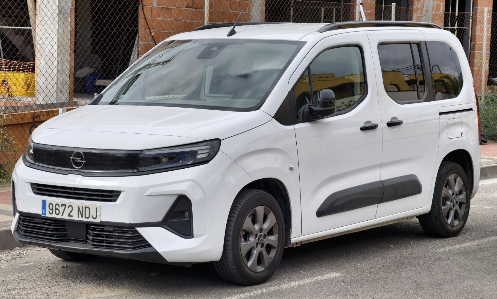 White MPV with modern headlights and aerodynamic design, front-side view.