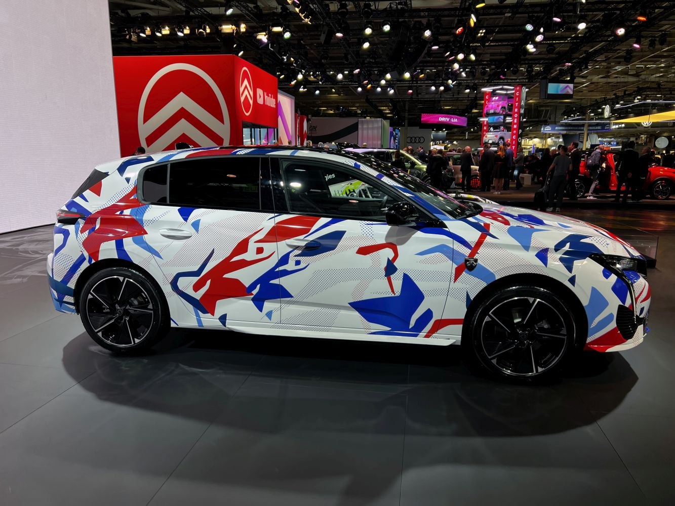 Hatchback side view with red and blue abstract camouflage and black alloy wheels.