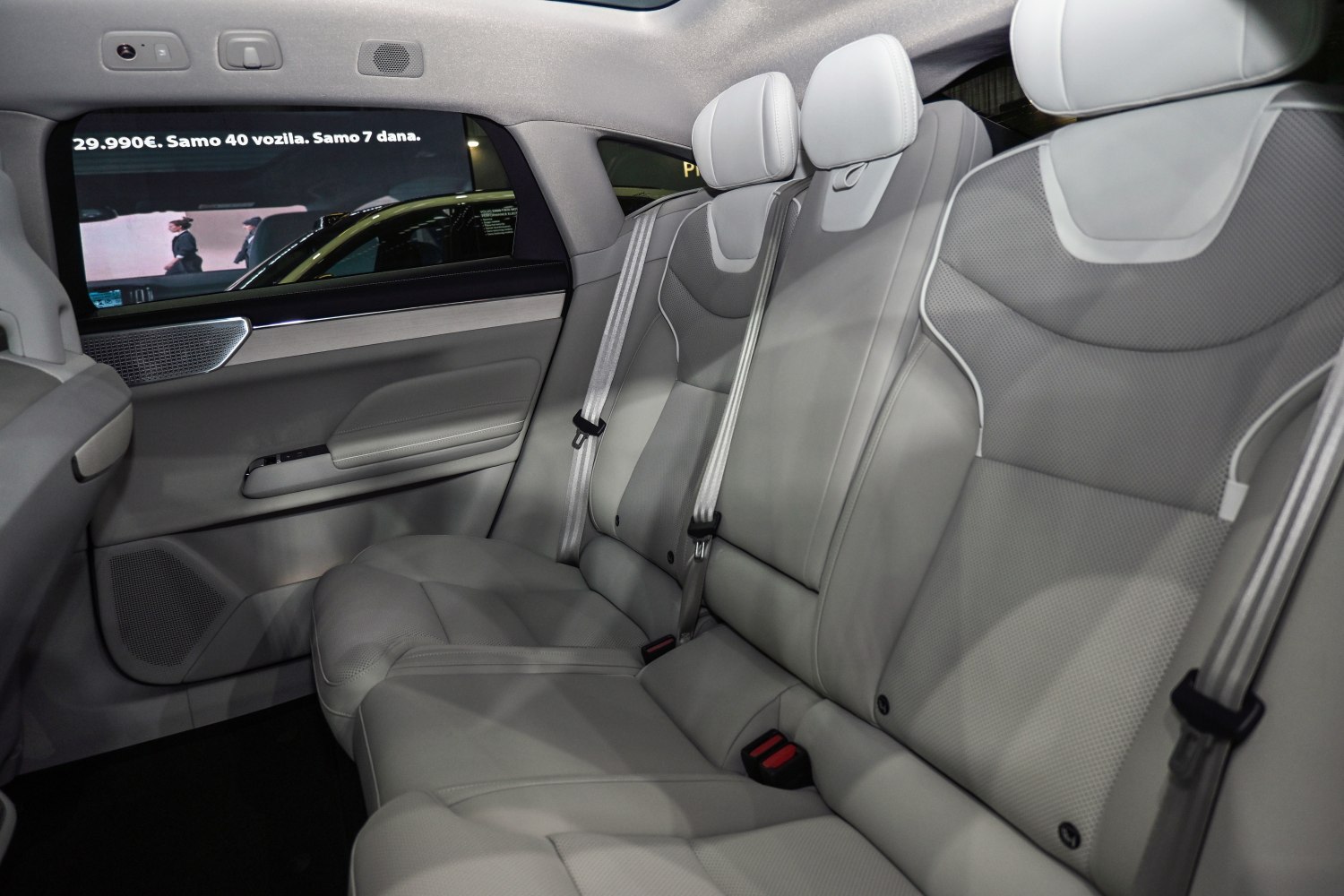 Spacious light gray leather rear seats with seat belts in a modern car interior