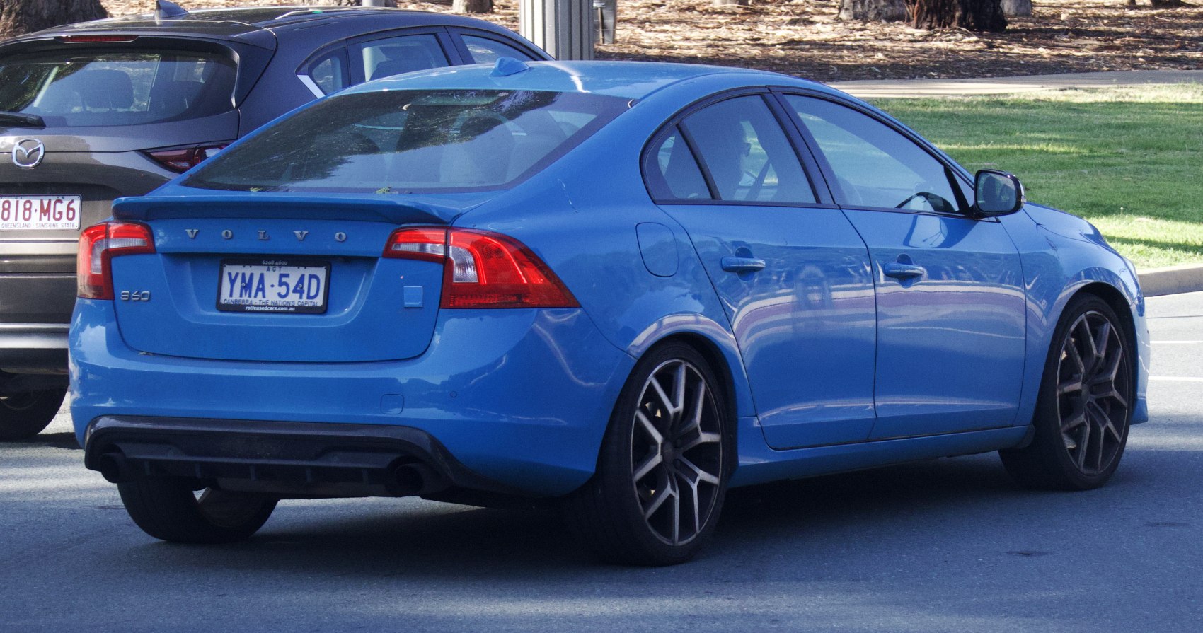 Rear side of blue sedan with tail lights, spoiler, and alloy wheels