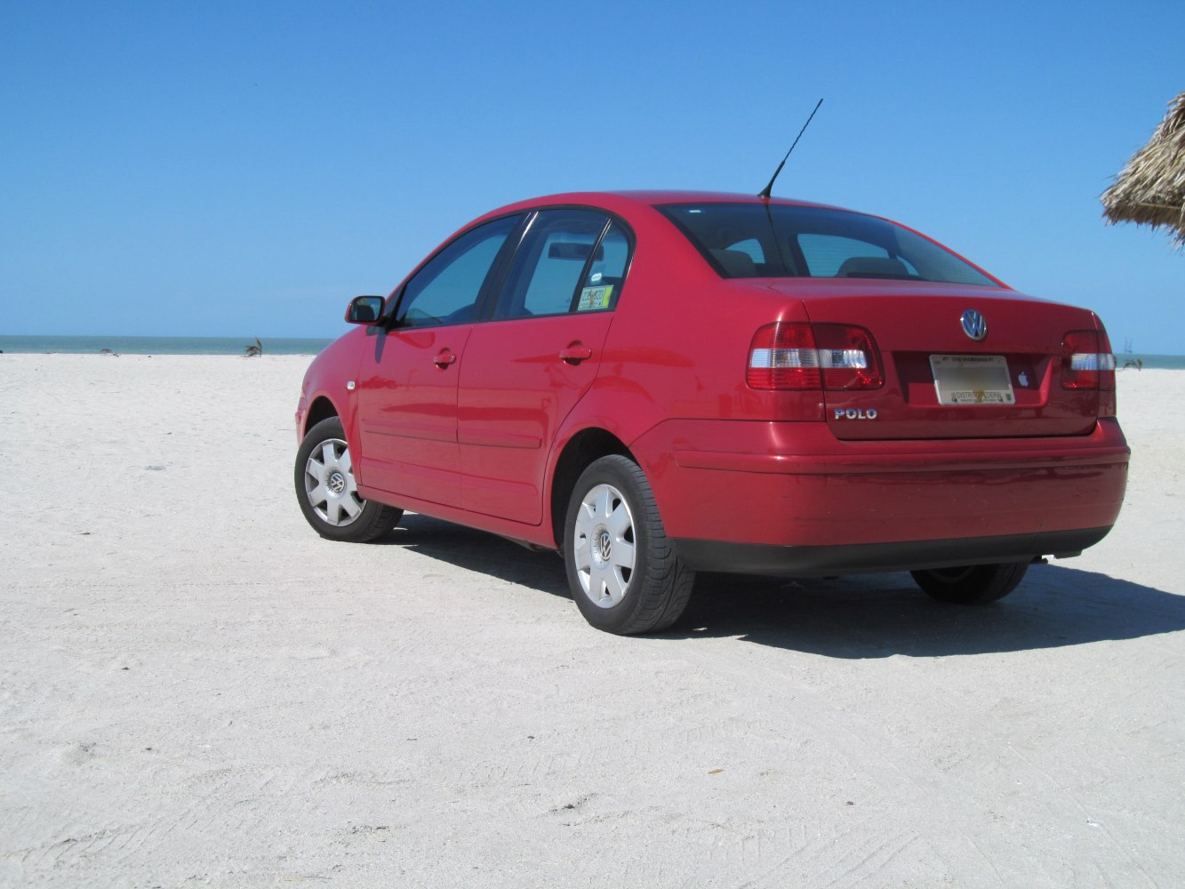 Rear side view of red sedan on sandy beach