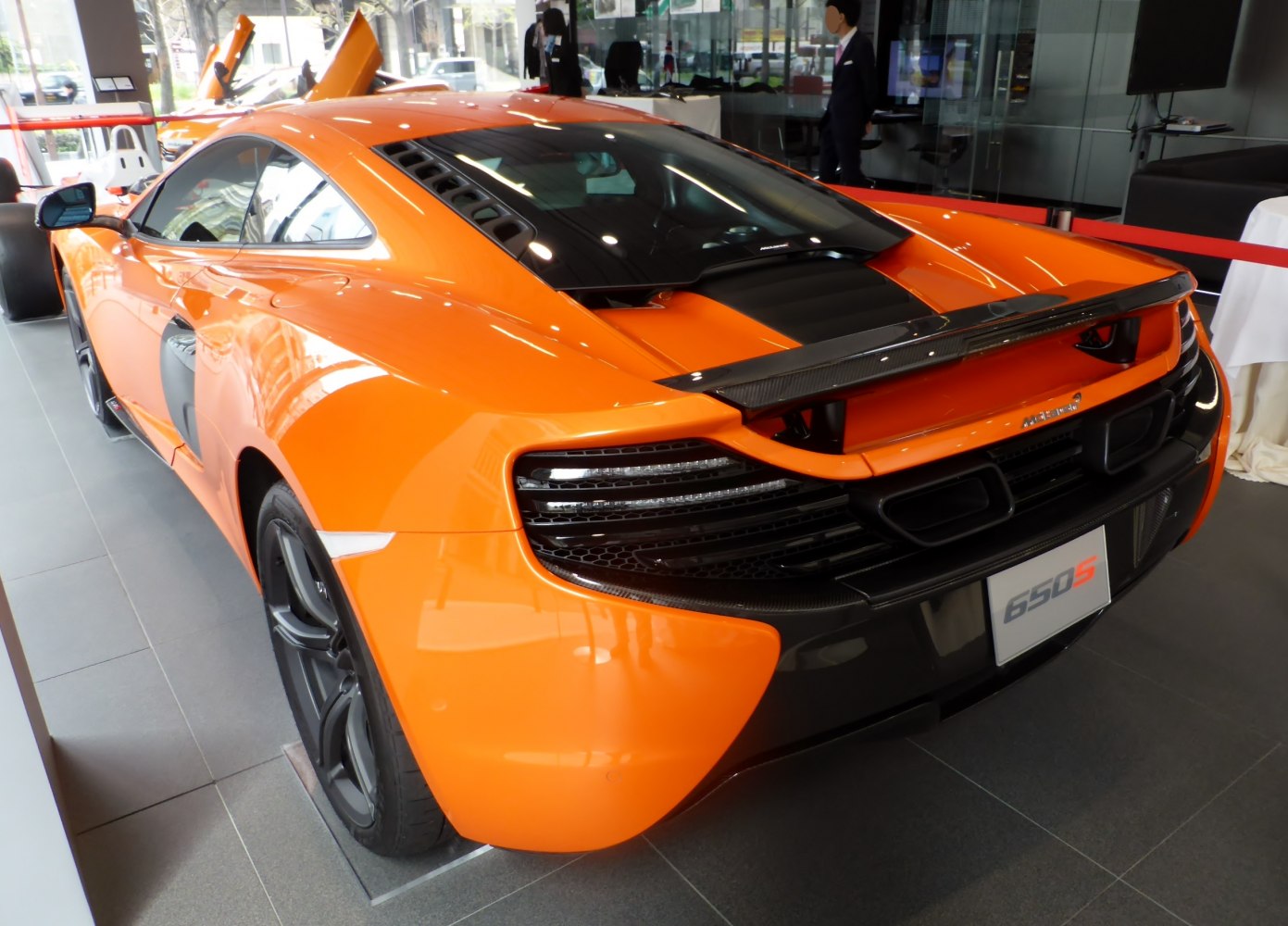 Rear view of a bright orange sports car with distinctive taillights and rear wing