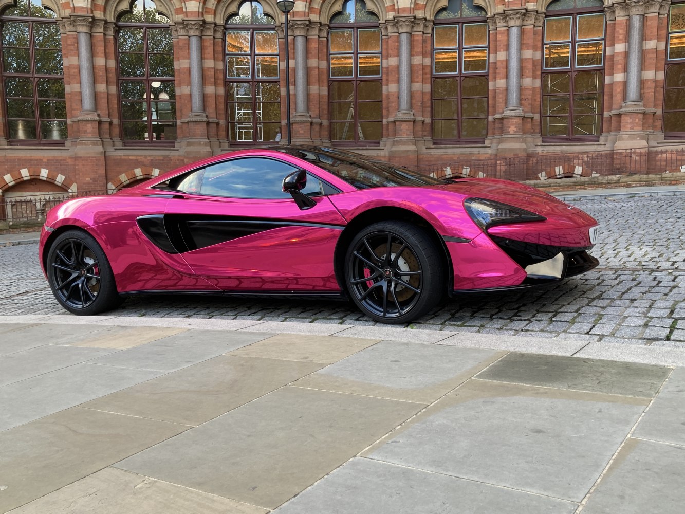 Side profile of a sleek car with pink chrome wrap and black accent details