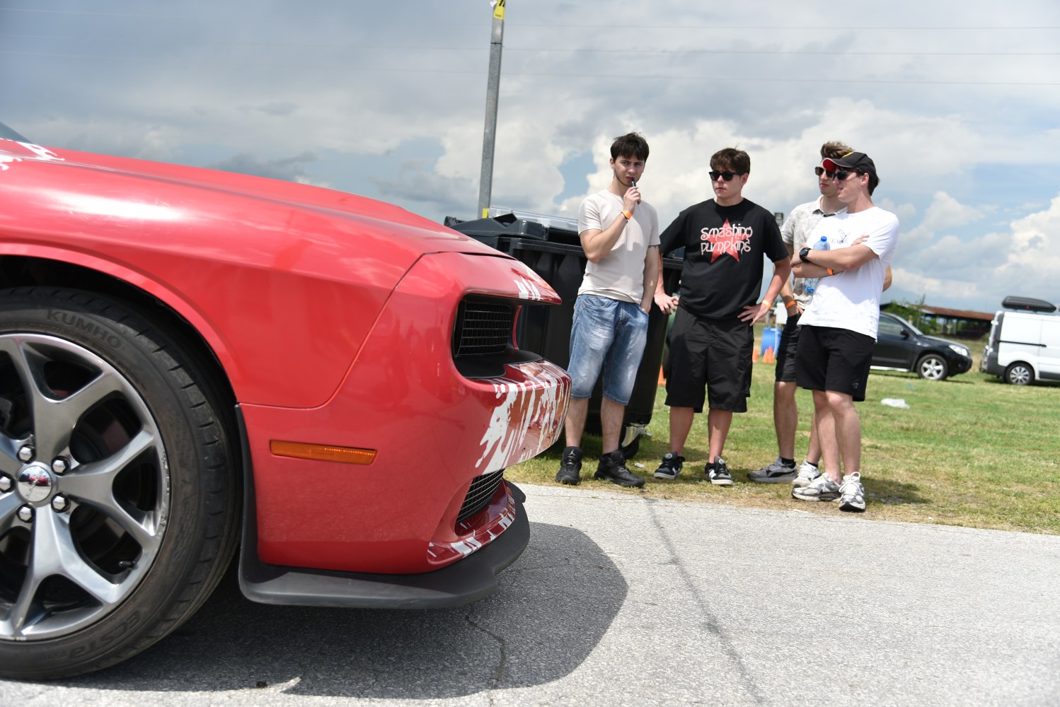 Close-up of red muscle car front, alloy wheels, group of young men outdoors