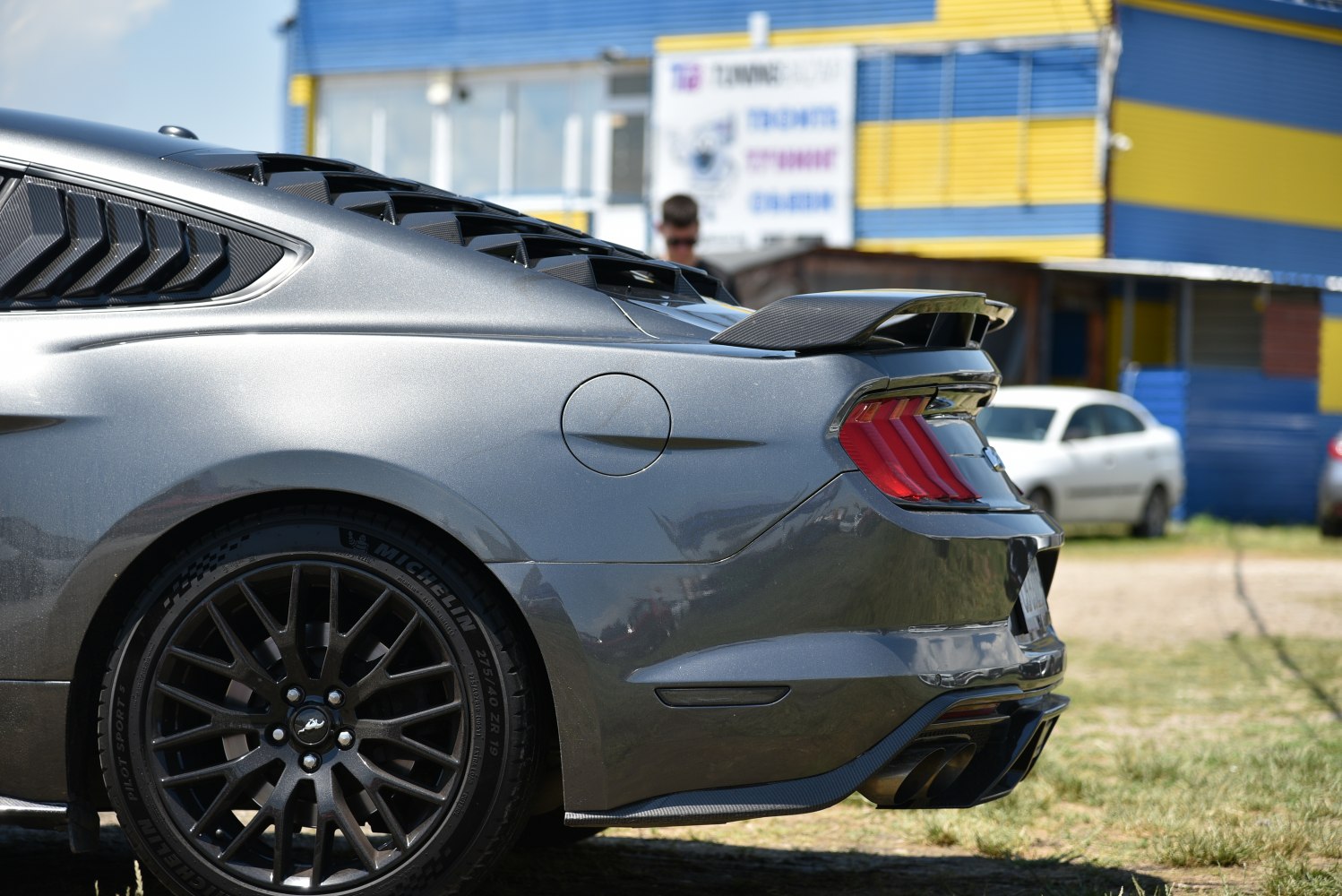 Rear quarter showing black alloy wheels, louvered rear window, carbon fiber spoiler.